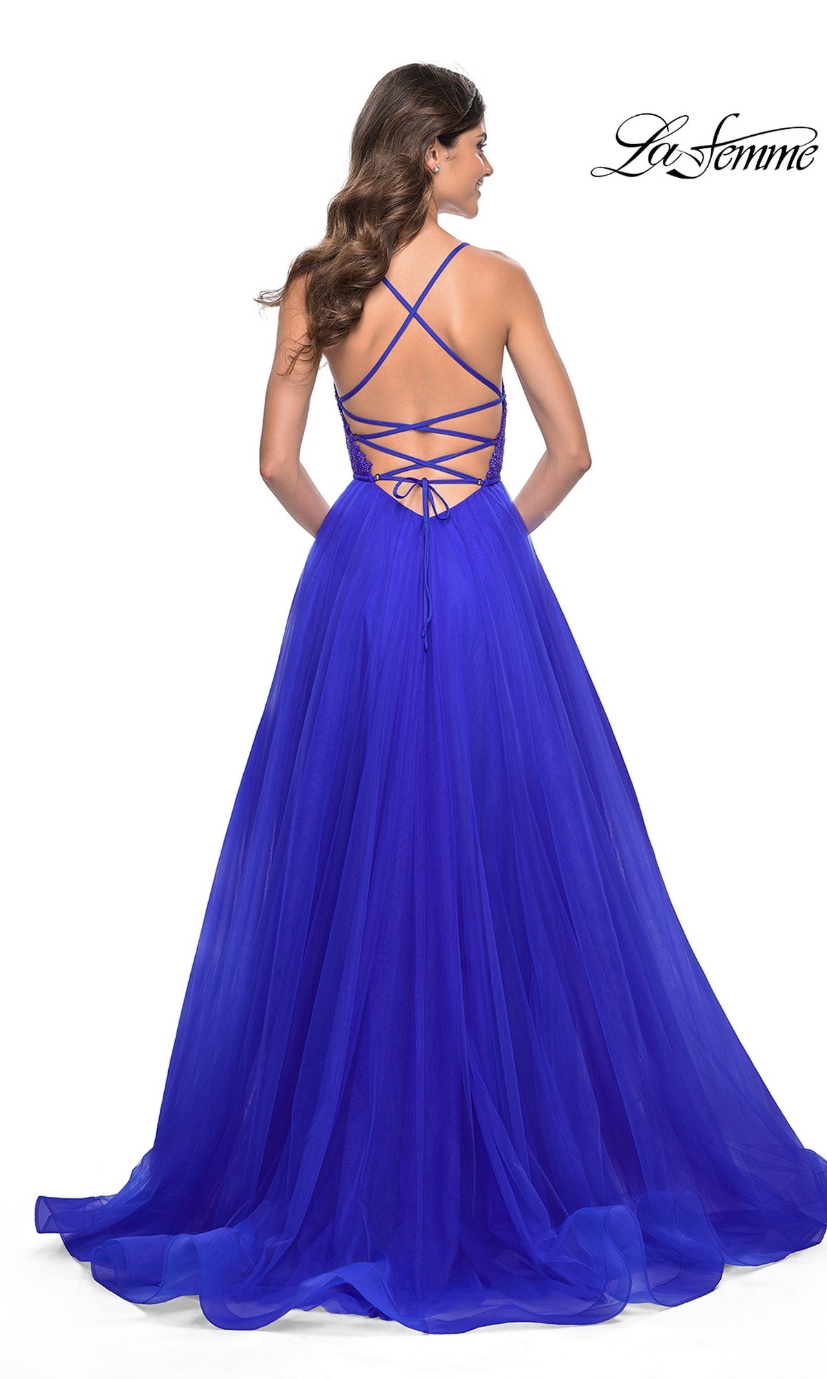 Woman wearing the La Femme Deep V-Neck Long Tulle Prom Gown 32059 in royal blue, featuring a lace bodice, strappy lace-up open back, and long tulle skirt, stands against a white background.